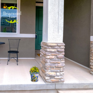 Small ceramic pot with yellow flowers on a house porch with stone pillar and green door.