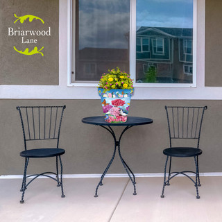 Geraniums in Bloom Medium Planter on a black metal table between two matching chairs outside.
