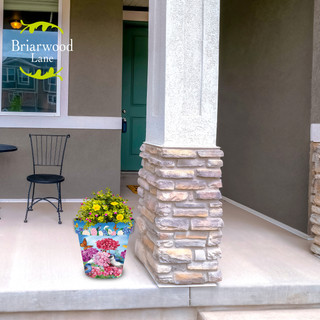 Vibrant colorful flowers in a medium sized planter on a home's porch with a stone pillar.