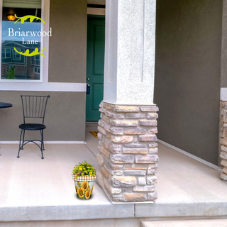 Small Sunflower Duo planter with green plants on a house porch next to pillar and chair.