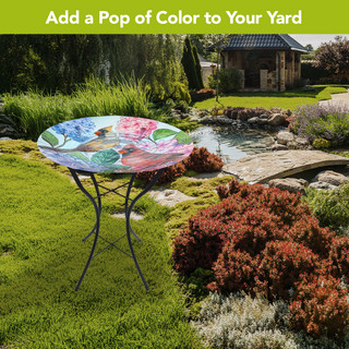 Perched Cardinals Glass Birdbath, colorful glass top with cardinals, flowers on black metal stand outdoors.
