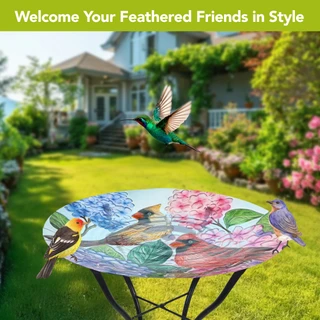 Perched Cardinals Glass Birdbath with colorful bird designs on a garden table outdoors with flowers.