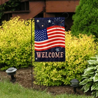 Burlap garden flag with American flag and welcome text on a garden stand outdoors.