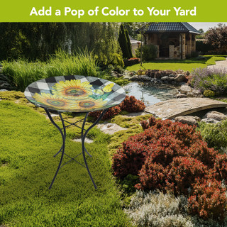 Checkered sunflowers summer glass birdbath on stand with black metal legs in a garden setting outdoors.