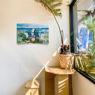 Seaside Escape Large LED Canvas Art on wall above wooden table with plant and window.