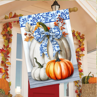 Blue and white pumpkins house flag with floral bow on a porch with fall decorations displayed.