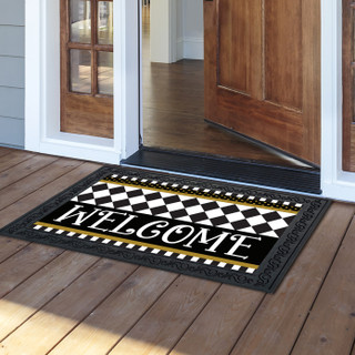 Black and white checkerboard doormat with gold accents and welcome text on wooden porch floor.