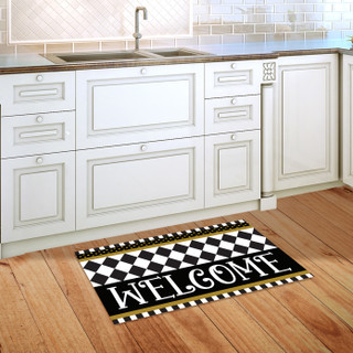 Black and white checkerboard doormat with welcome text on wooden kitchen floor beside white cabinets.