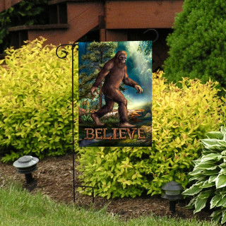 Believe Bigfoot garden flag with colorful Sasquatch design and text on a black metal stand outdoors.