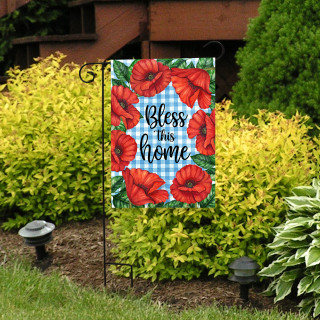 Bless This Home garden flag with red poppies on blue plaid background and green leaves displayed outdoors.
