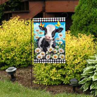 Black and white cow garden flag with checkered border and white daisies on a garden stand.