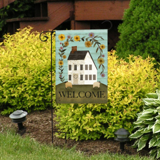 Country Saltbox Garden Flag with white house, sunflowers, and welcome text on a garden stand outside.
