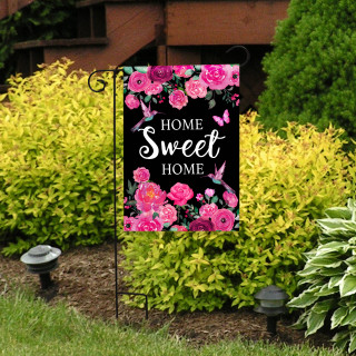 Home Sweet Home garden flag with pink flowers and hummingbirds on a black background outdoors.