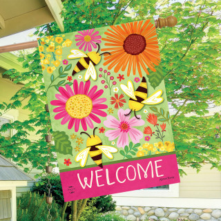 Buzzing Blooms House Flag with colorful flowers, bees, and welcome text on pink background hanging outdoors.