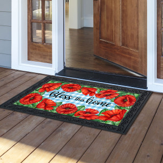 Bless This Home checkered floral doormat with red poppies on wooden porch outside open door.