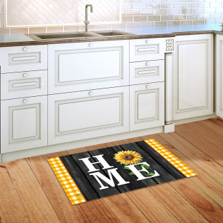 Black doormat with yellow sunflower and "HOME" on wooden floor beside white kitchen cabinets.