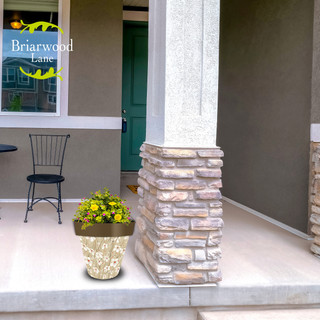 Tan and red floral medium planter with yellow flowers on a porch next to a pillar.
