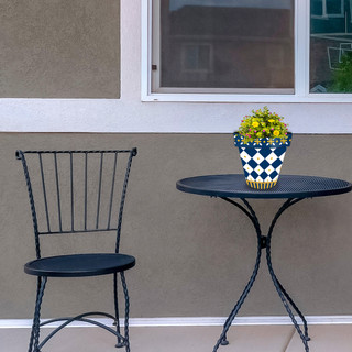 Small blue and gold planter with yellow flowers on a black metal table beside a chair.
