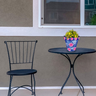 Small pink and blue tropical planter on a black metal table next to a chair outdoors.