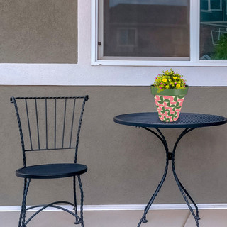 Pink and green modern planter on small black metal table beside matching chair outdoors.