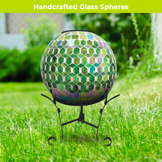 Green and purple solar LED glass gazing ball on black metal stand outdoors on grass.