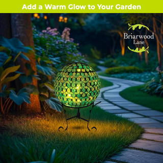 Green and purple solar LED glass gazing ball on stand in garden with warm glowing light.