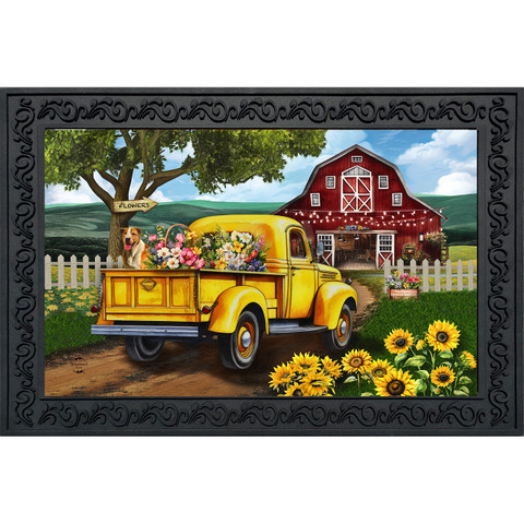 Vibrant yellow vintage truck loaded with colorful flowers beside sunflowers and red barn with white fence.