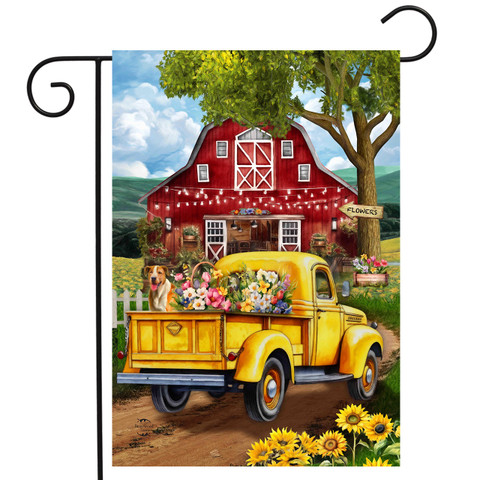 Yellow vintage truck with flowers, parked in front of red barn on garden flag.