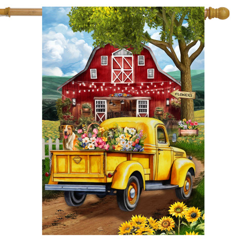 Yellow vintage truck with flowers and dog, parked in front of red barn house flag.