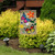 Briarwood Lane burlap garden flag with colorful butterfly and flower design on a garden stand outdoors.