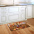 Briarwood Lane Autumn Scarecrow Harvest Doormat on wooden kitchen floor beside white cabinets and sink.