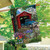 Briarwood Lane Bridge in Blooms Spring House Flag with colorful, printed, covered bridge design on porch.