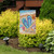 Briarwood Lane small printed garden flag with colorful beach scene and welcome message on a lawn.