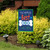 Briarwood Lane double-sided garden flag with colorful dog design and pawprint on blue background displayed outdoors.