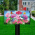Briarwood Lane Geraniums In Bloom mailbox cover with colorful flowers, butterflies, and birds on a lawn.