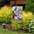Briarwood Lane garden flag with bluebirds, colorful flowers, and toolbox on a wooden background outdoors.