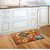 Briarwood Lane Fall Floral Birdhouses Doormat on wooden floor beside kitchen sink and white cabinets.