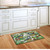 Briarwood Lane Winter Chickadees Doormat on wooden floor in front of white kitchen cabinets.
