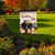 Black truck garden flag with Welcome Fall text and autumn decorations on a lawn pole outdoors.