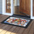Holiday Cheer Dogs Doormat with colorful dog and house design on wooden porch outside doorway.