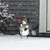 Checkered snowman metal art with hat and scarf holding bird on snowy yard near house.