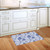 Blue and white floral doormat on wooden floor beside kitchen sink and white cabinets.