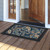 Paisley doormat with black border and colorful paisley design on wooden porch outside open doorway.