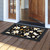 Elegant Flowers Doormat with white flowers and green leaves on a black background outside doorway.