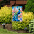 Fancy Peacock Garden Flag with colorful peacock and flowers on a garden stand outdoors.