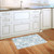 Blue and white ornamental doormat on wooden floor in front of kitchen sink and cabinets.