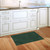 Green Tropical Leaves Doormat on wooden floor beside white kitchen cabinets and sink area.