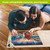 Couple working on Briarwood Lane Beachfront Fireworks Summer 1000-piece jigsaw puzzle on wooden floor together.