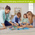 Family assembling Summer Gnomes 1000 piece jigsaw puzzle on floor together with puzzle pieces scattered around.