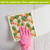 Pineapples and Leaves Swedish Dishcloth with pink glove on a white surface.